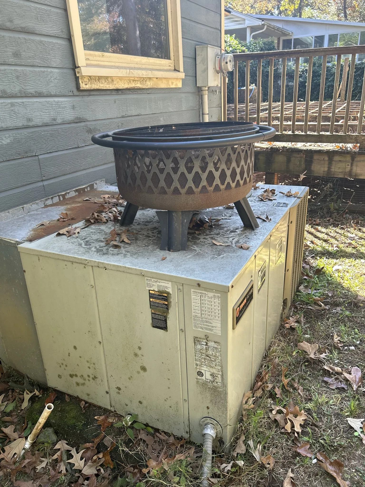 An old outdoor air conditioning unit sitting in a yard with a fire pit on top