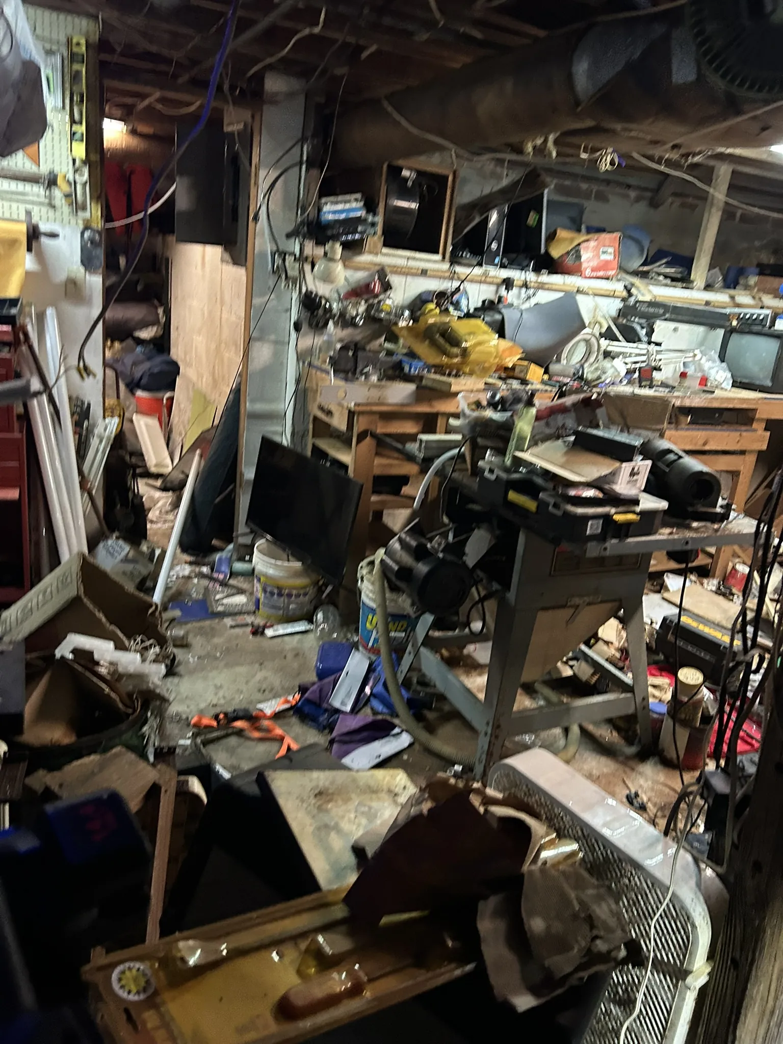 A cluttered basement workshop with tools, a workbench and an old TV