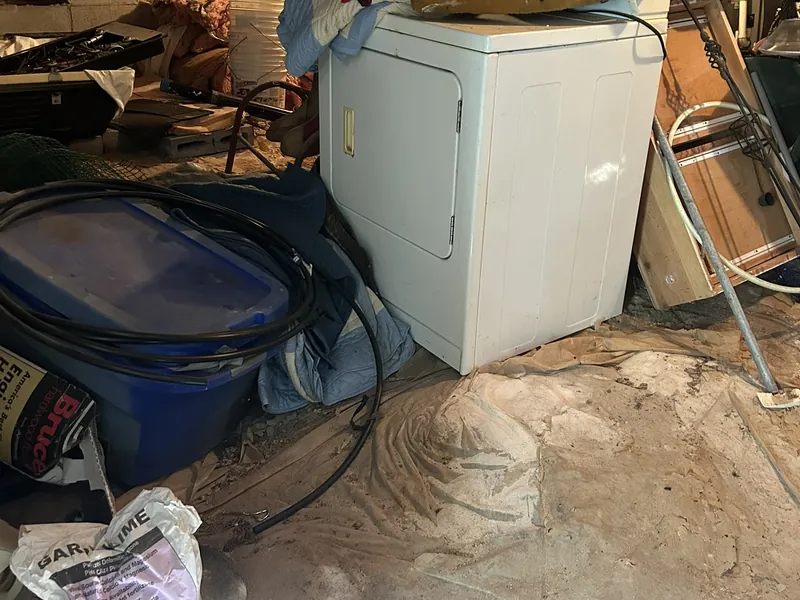 An old dryer and clutter under the ductwork of a basement