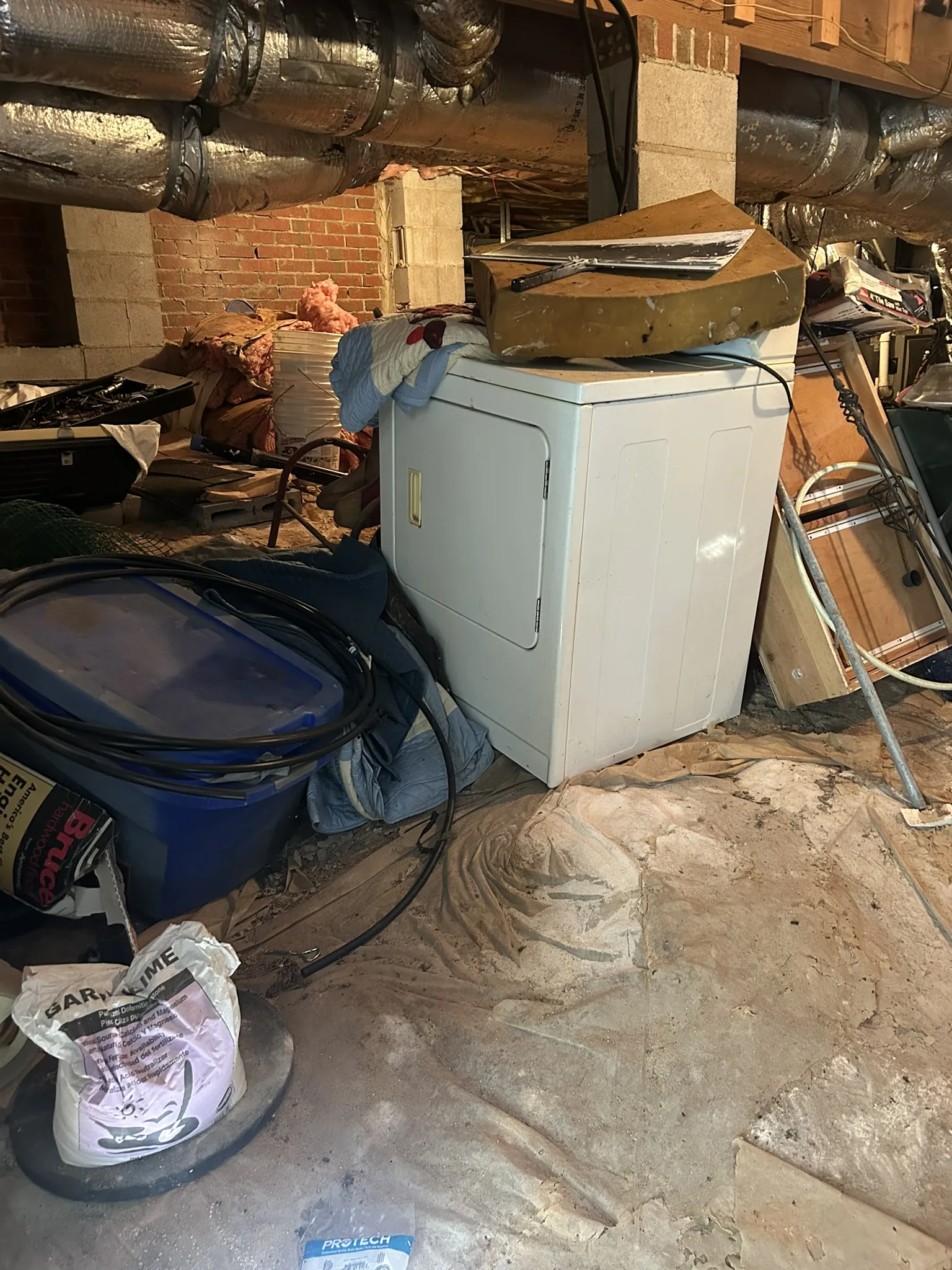 An old dryer and clutter under the ductwork of a basement