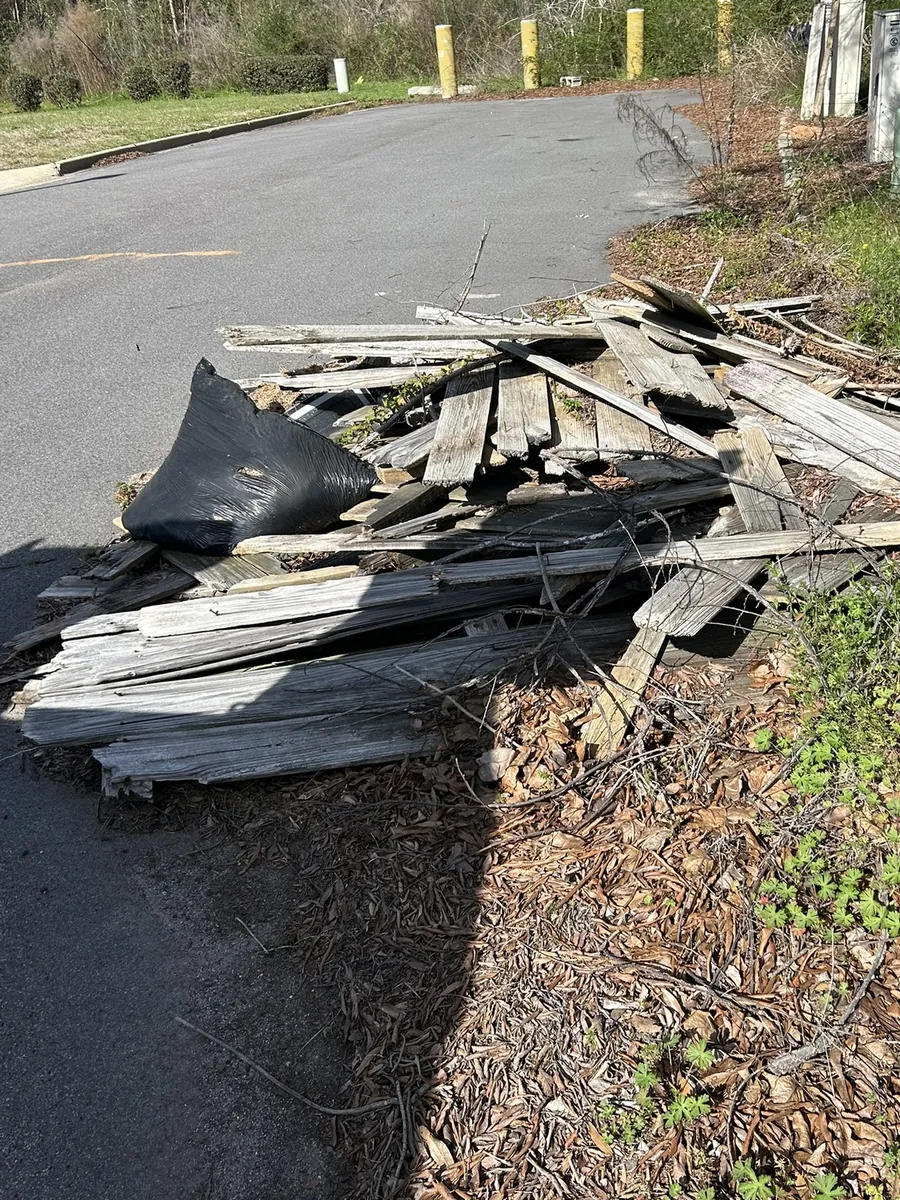 A pile of old boards and roofing debris along a paved lot