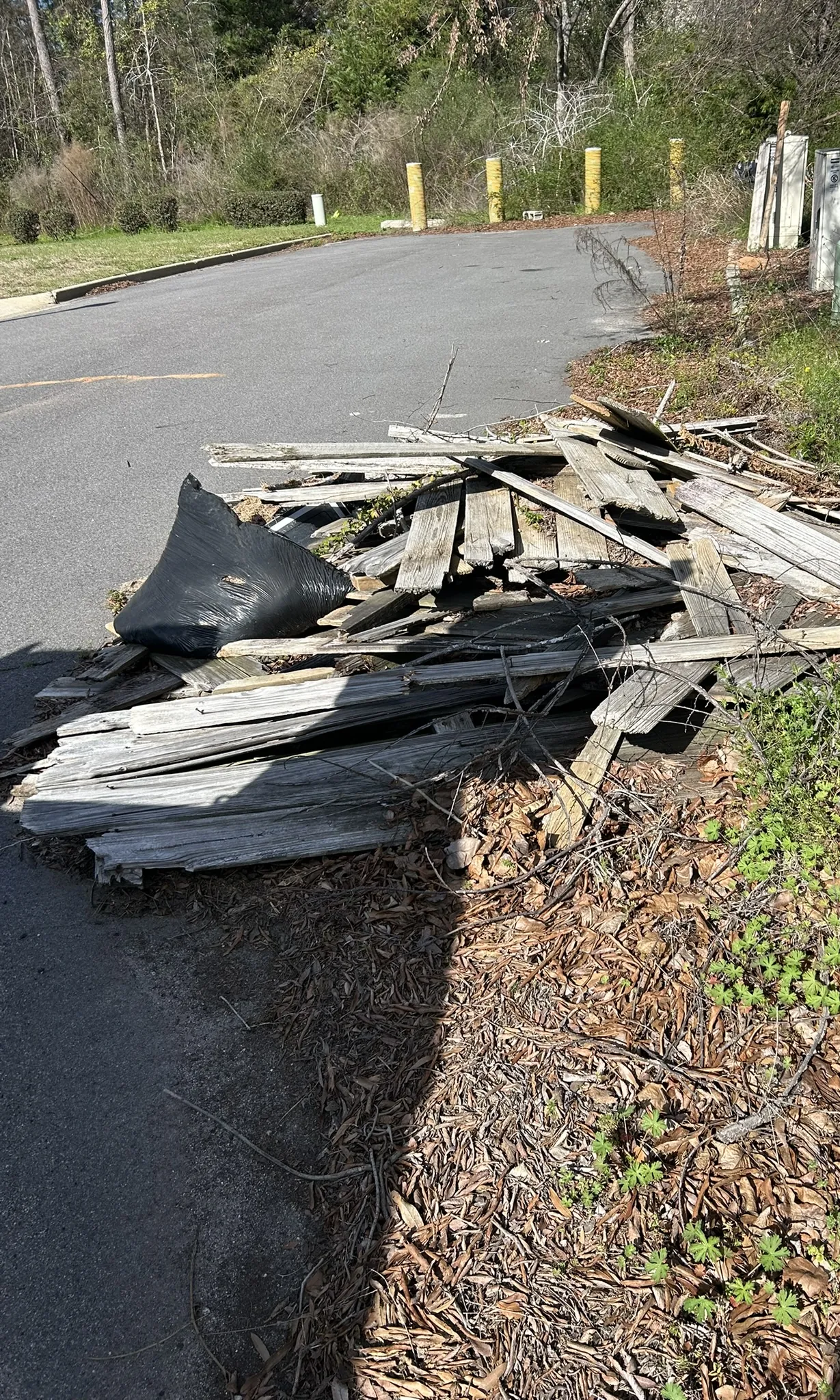 A pile of old boards and roofing debris along a paved lot