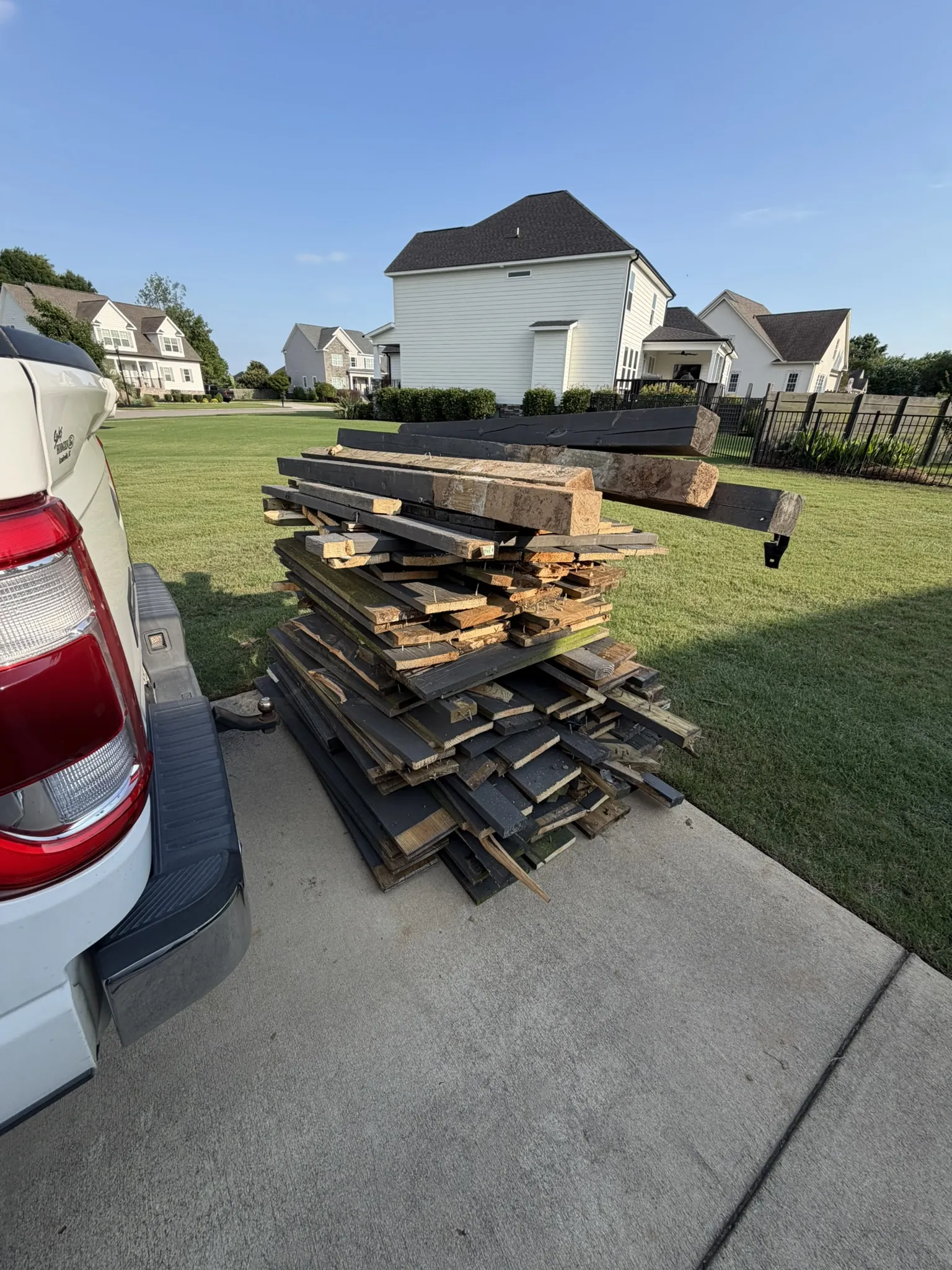 A stack of old lumber and boards on a driveway beside a pickup