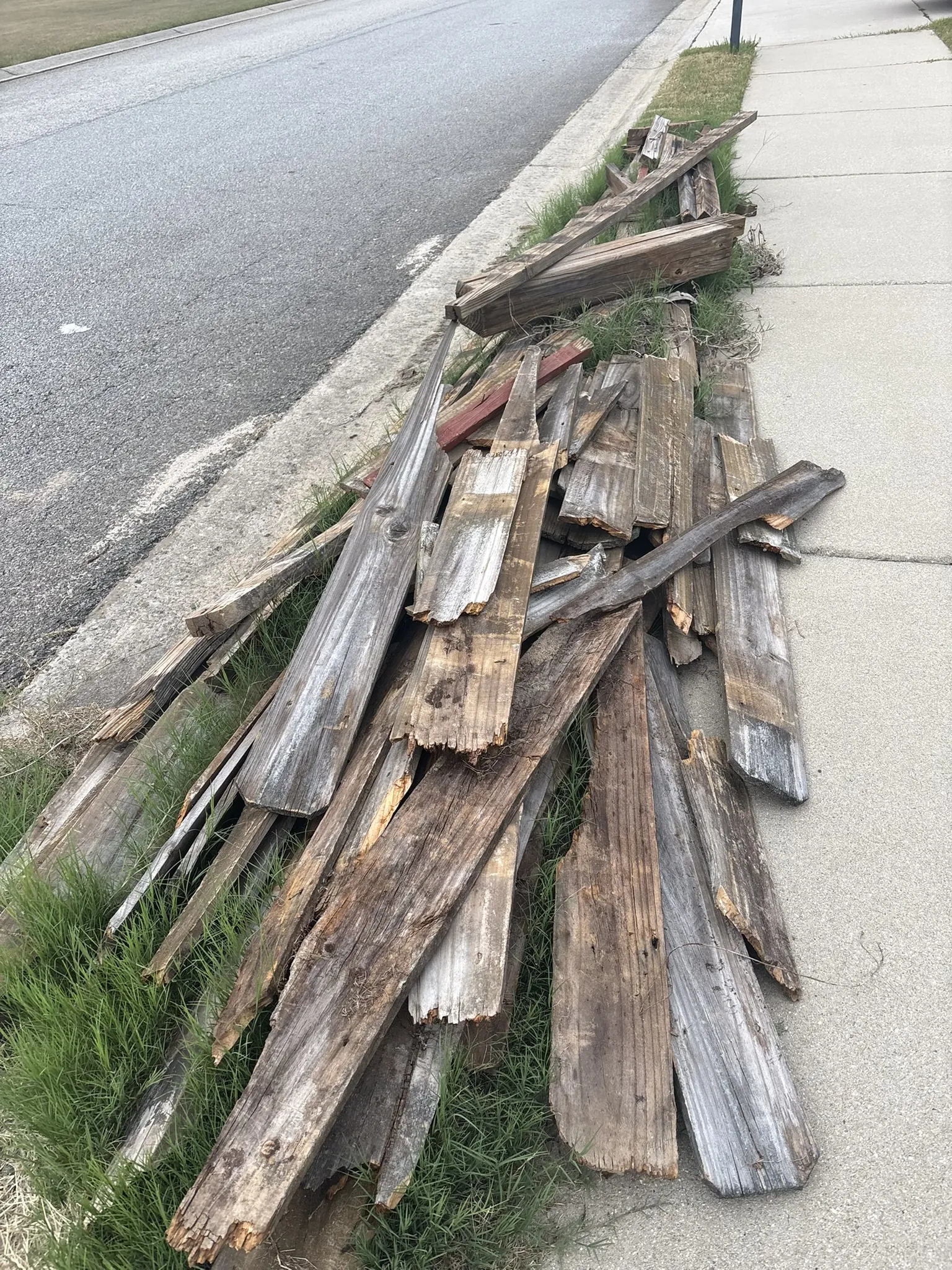 A pile of old weathered boards stacked along the curb