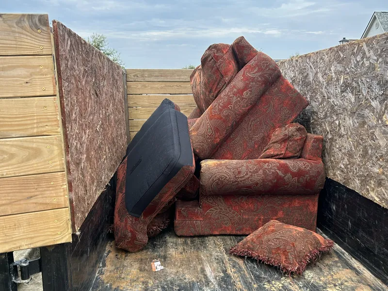 A red patterned couch and chair loaded in the dump trailer