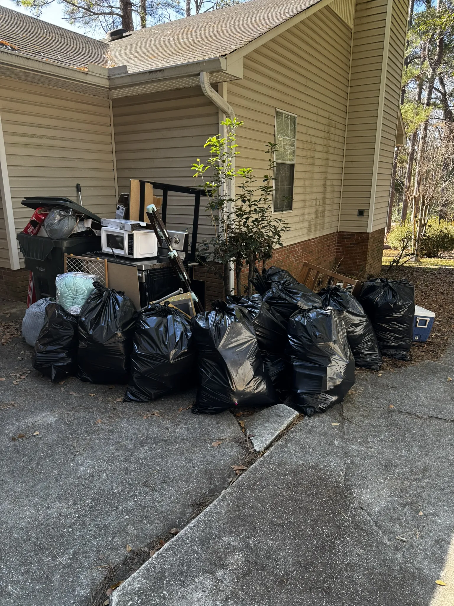 Trash bags, a microwave and household items stacked beside a house