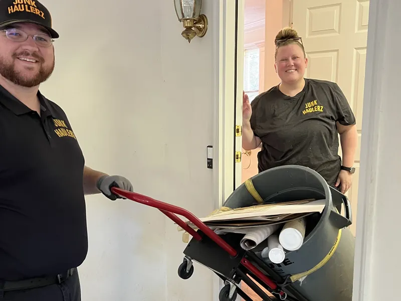 Pat Boatwright and a crew member moving a bin out of a house on a hand truck
