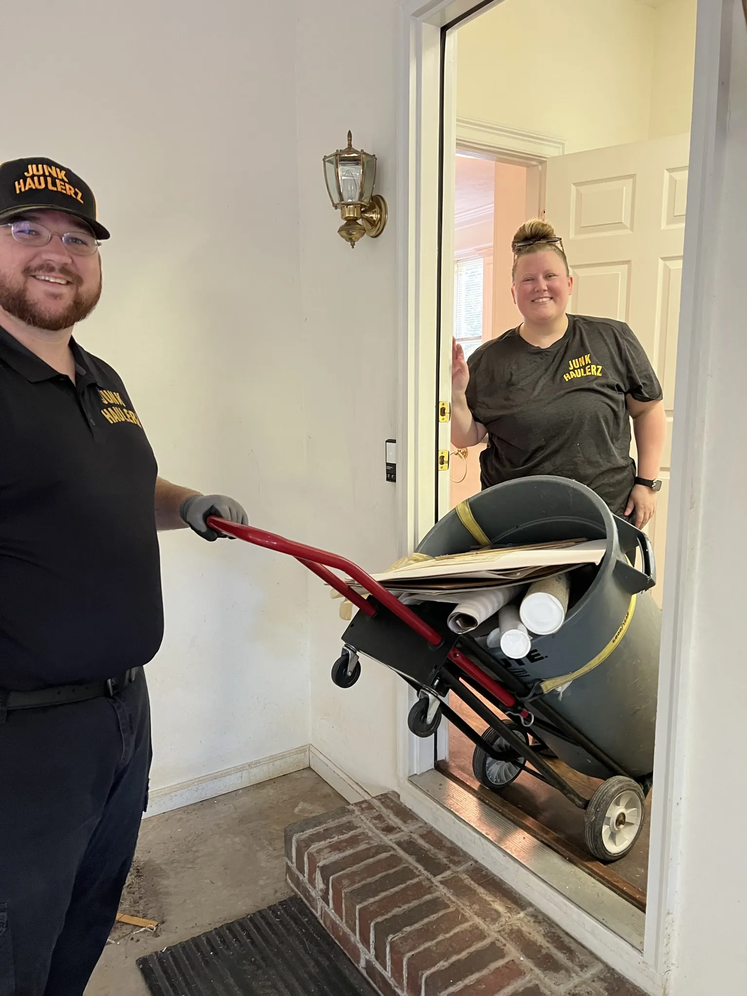 Pat Boatwright and a crew member moving a bin out of a house on a hand truck