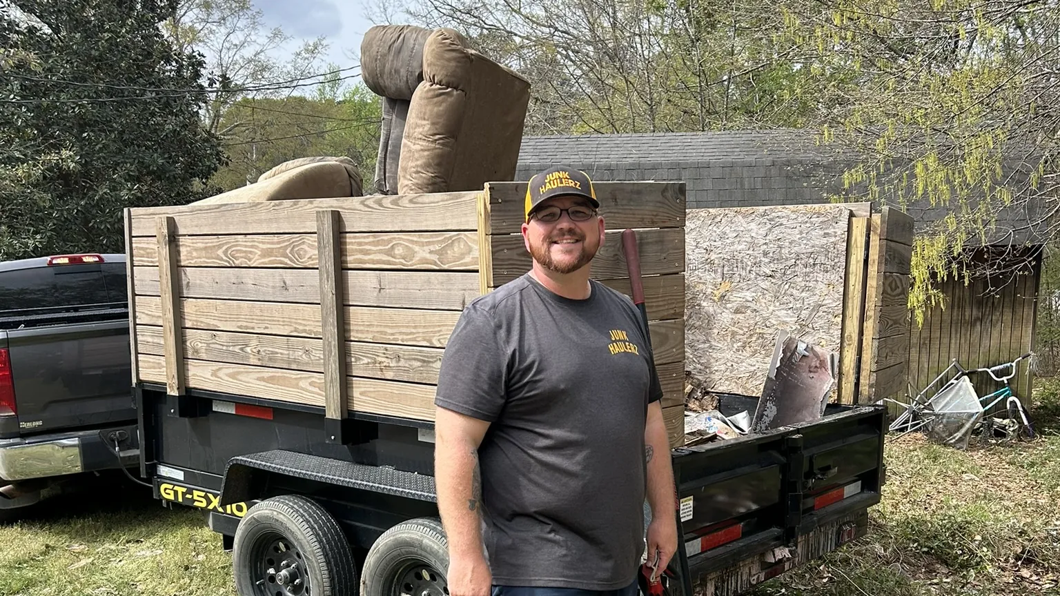 Pat Boatwright smiling beside his loaded dump trailer, a recliner on top