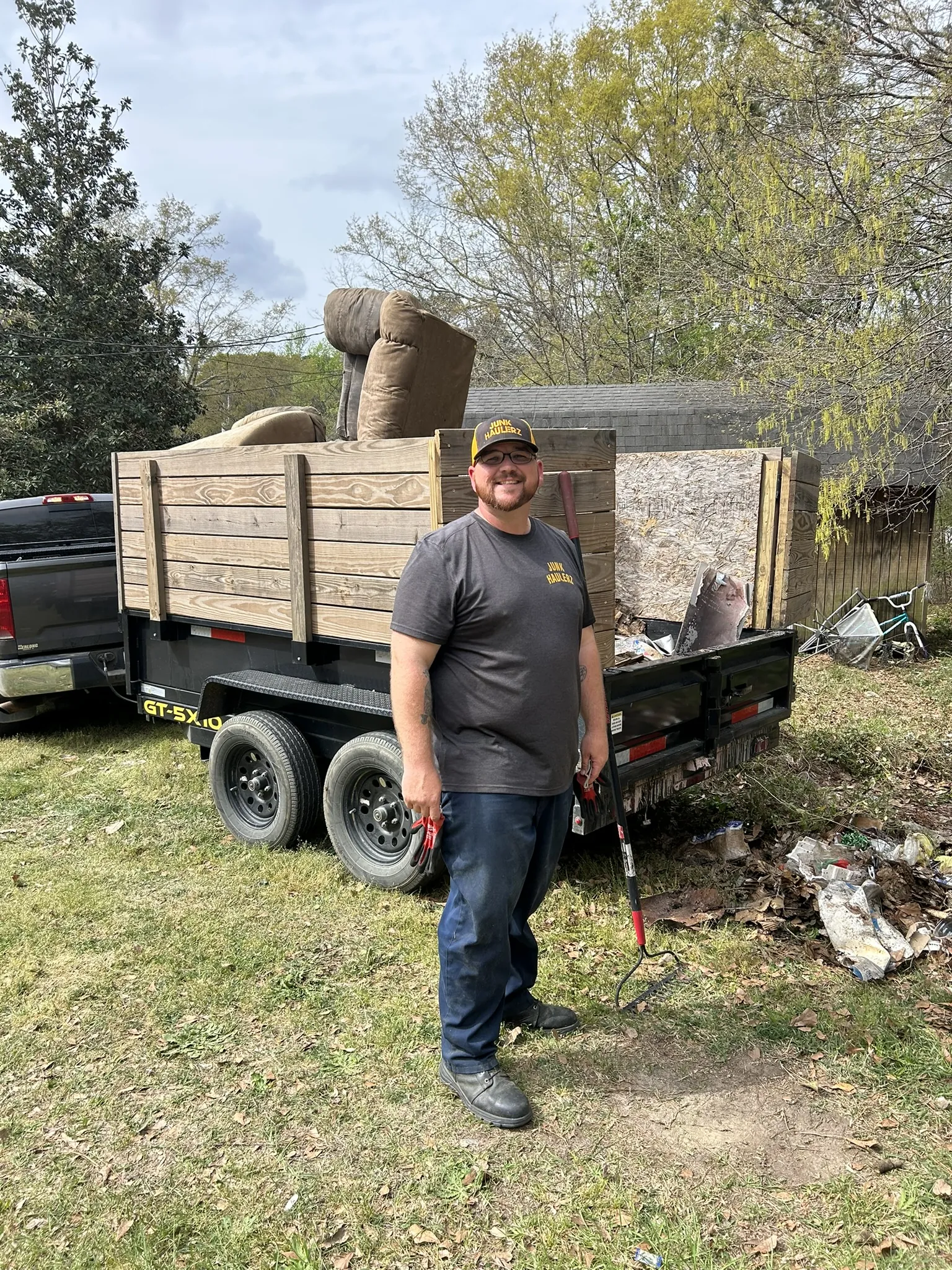 Pat Boatwright smiling beside his loaded dump trailer, a recliner on top