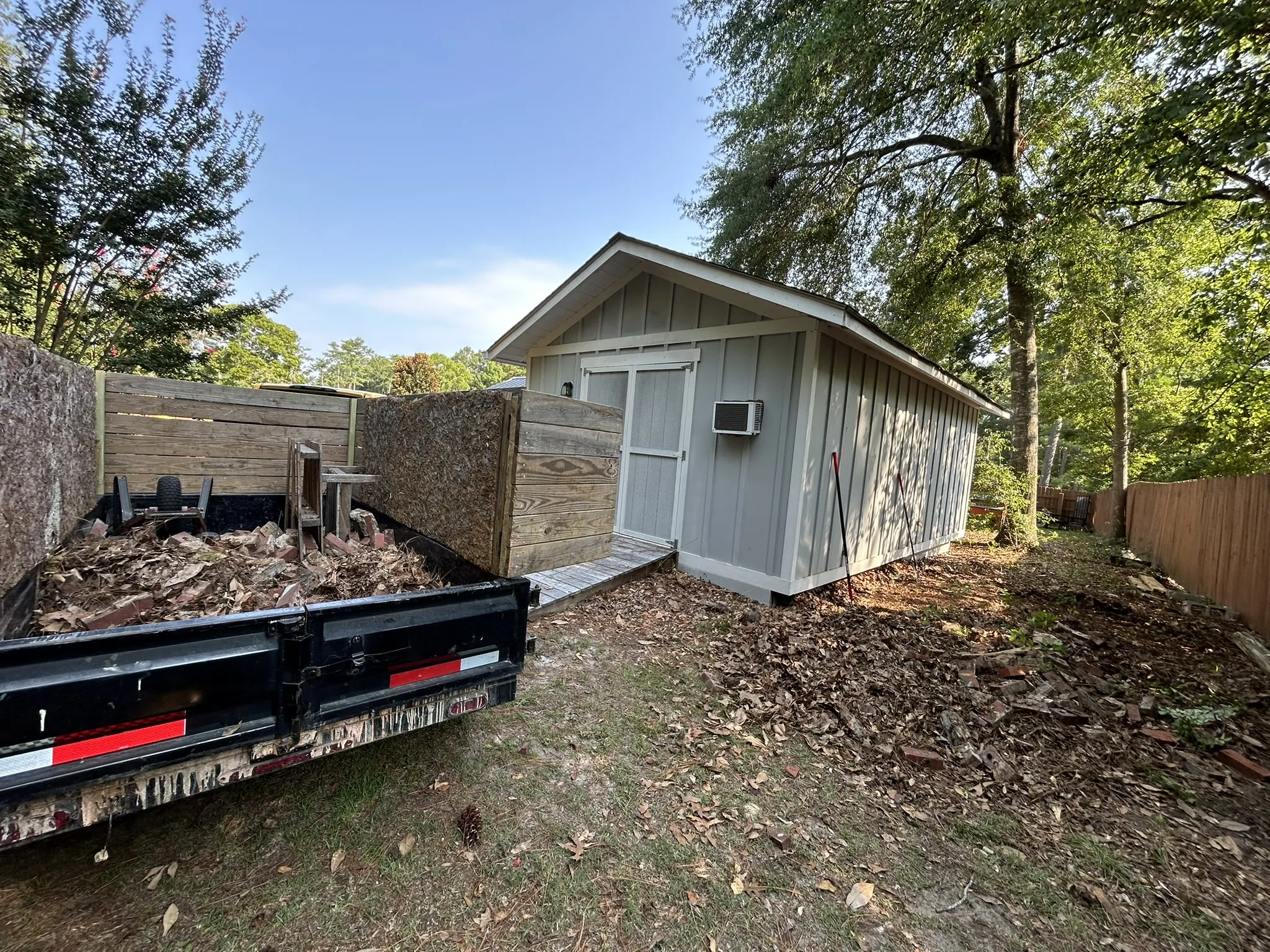 The dump trailer loaded with wood debris beside a backyard shed