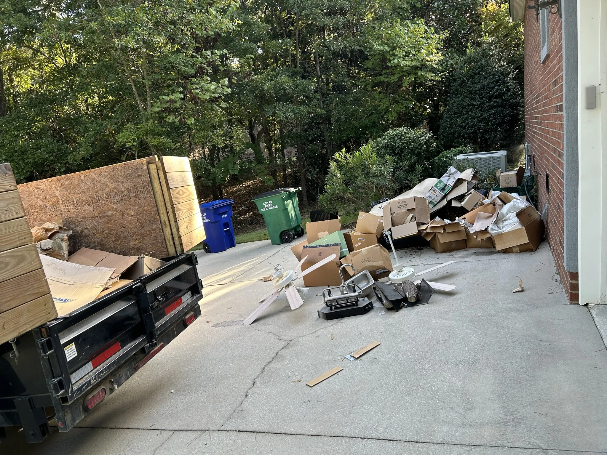 Empty boxes and ceiling fans piled on a driveway beside the dump trailer