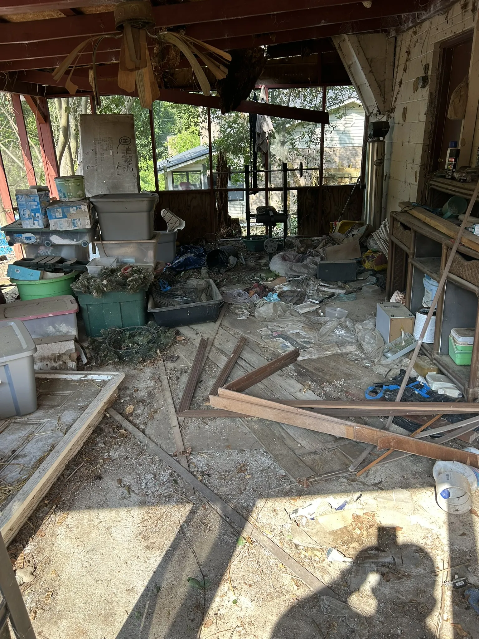 A covered carport cluttered with boards, bins and household items