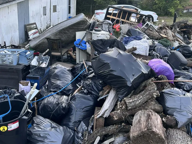 A huge pile of trash bags, logs and furniture beside a house
