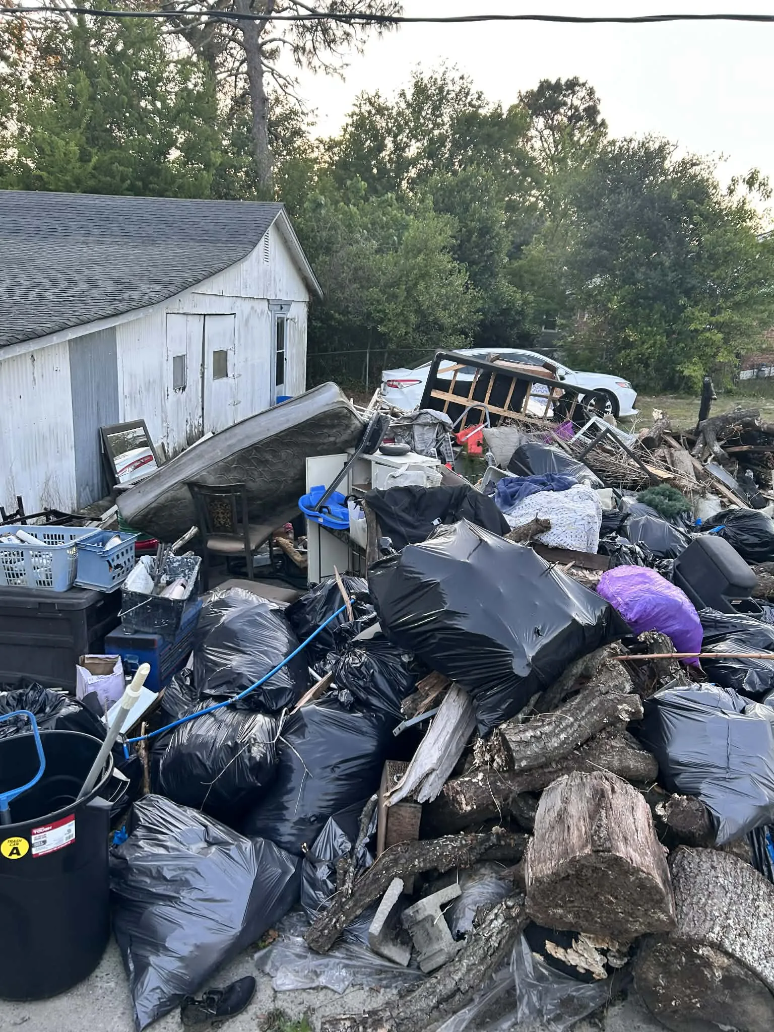 A huge pile of trash bags, logs and furniture beside a house