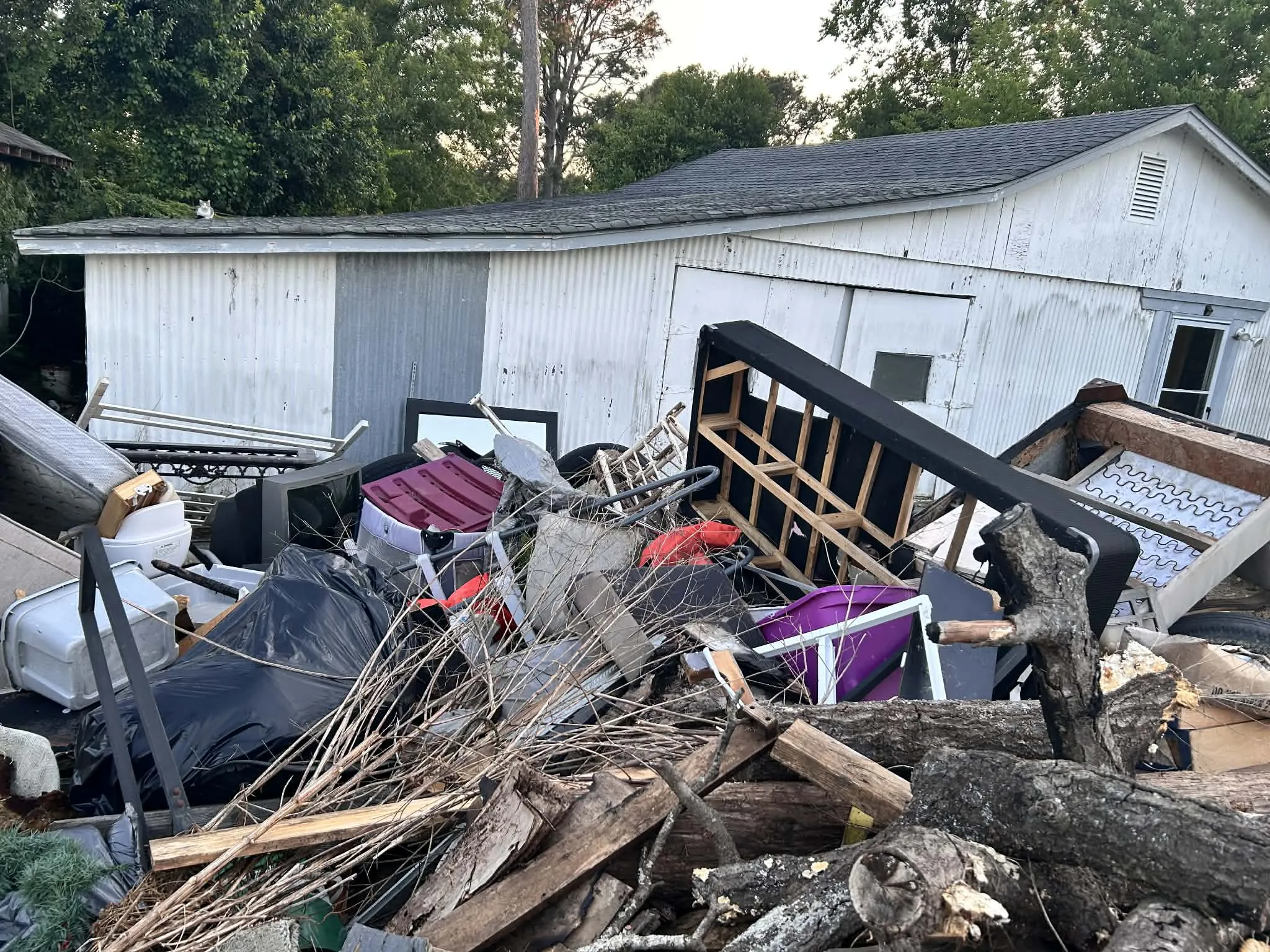 A large pile of furniture, a bed frame, bags and branches beside a shed
