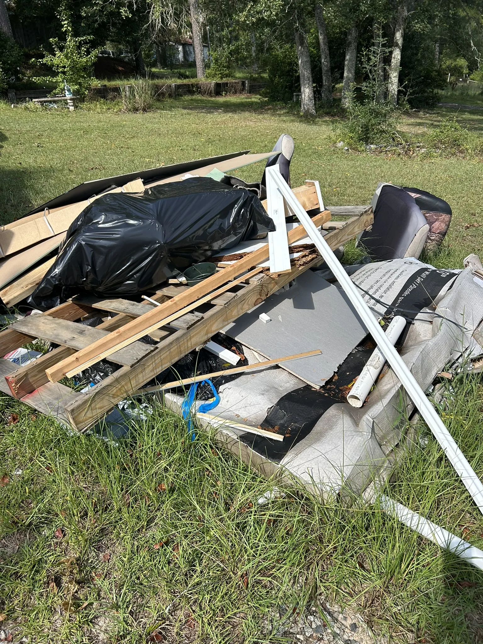 A pile of boards, a tarp and household items in a yard