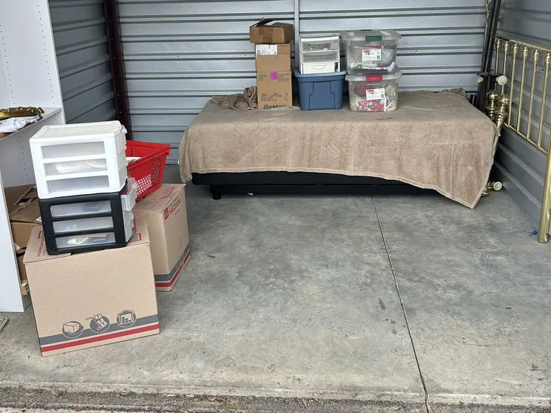 A storage unit with boxes, plastic drawers, a bed and a brass headboard