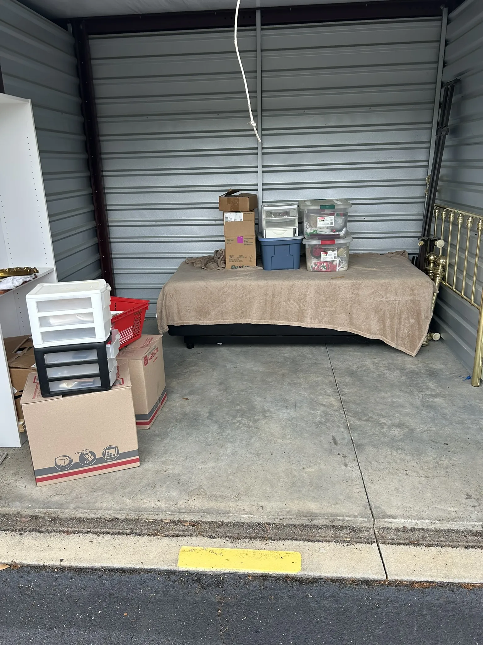 A storage unit with boxes, plastic drawers, a bed and a brass headboard